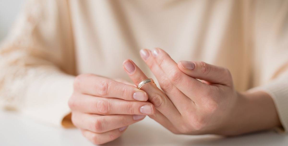 Women with tan shirt taking off her wedding ring.