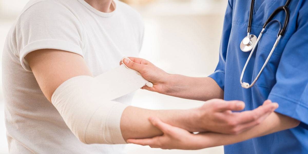 Nurse in blue scrubs wrapping on mans injured arm.