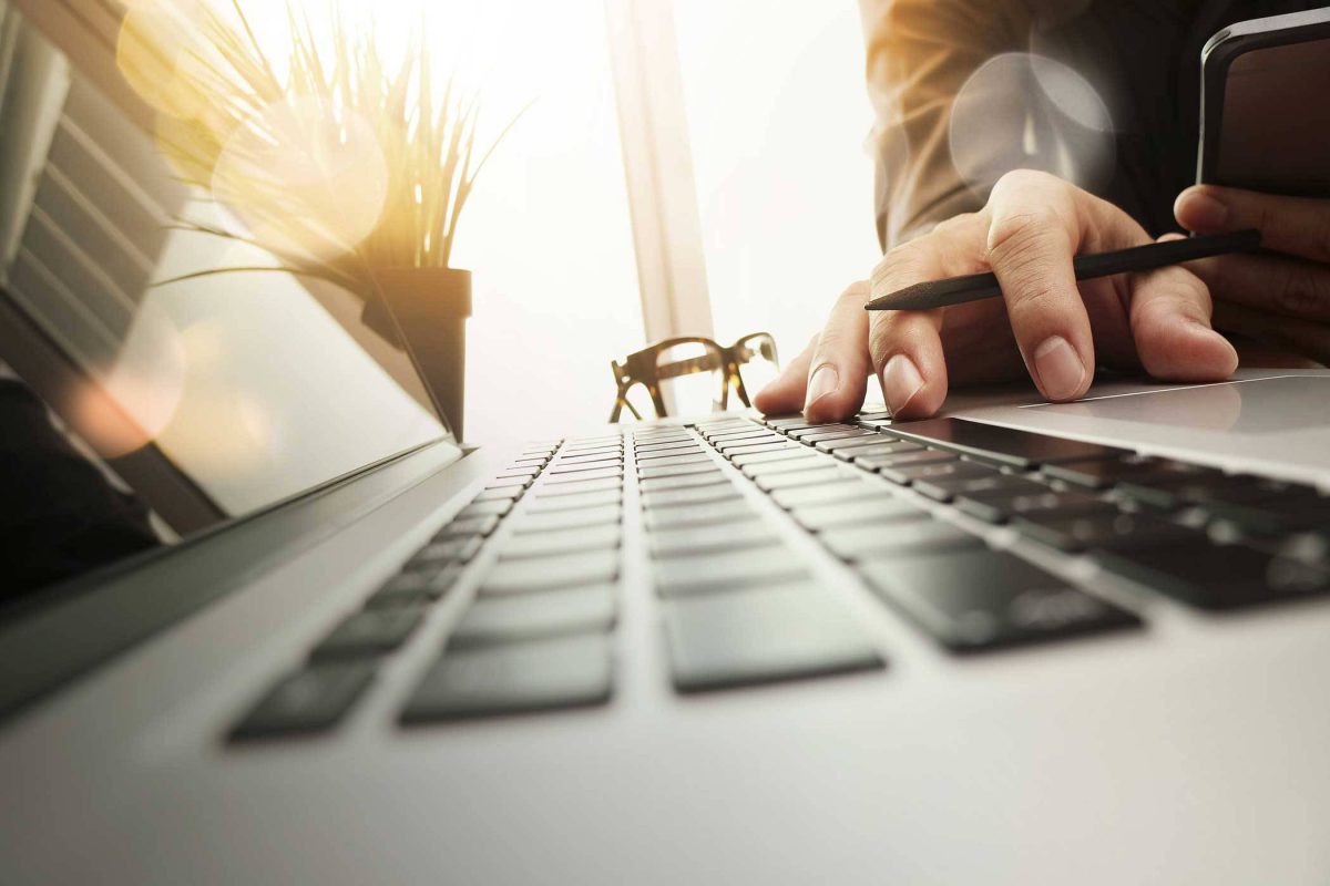 laptop sitting on a desk with a hand typing with sun shining in the background