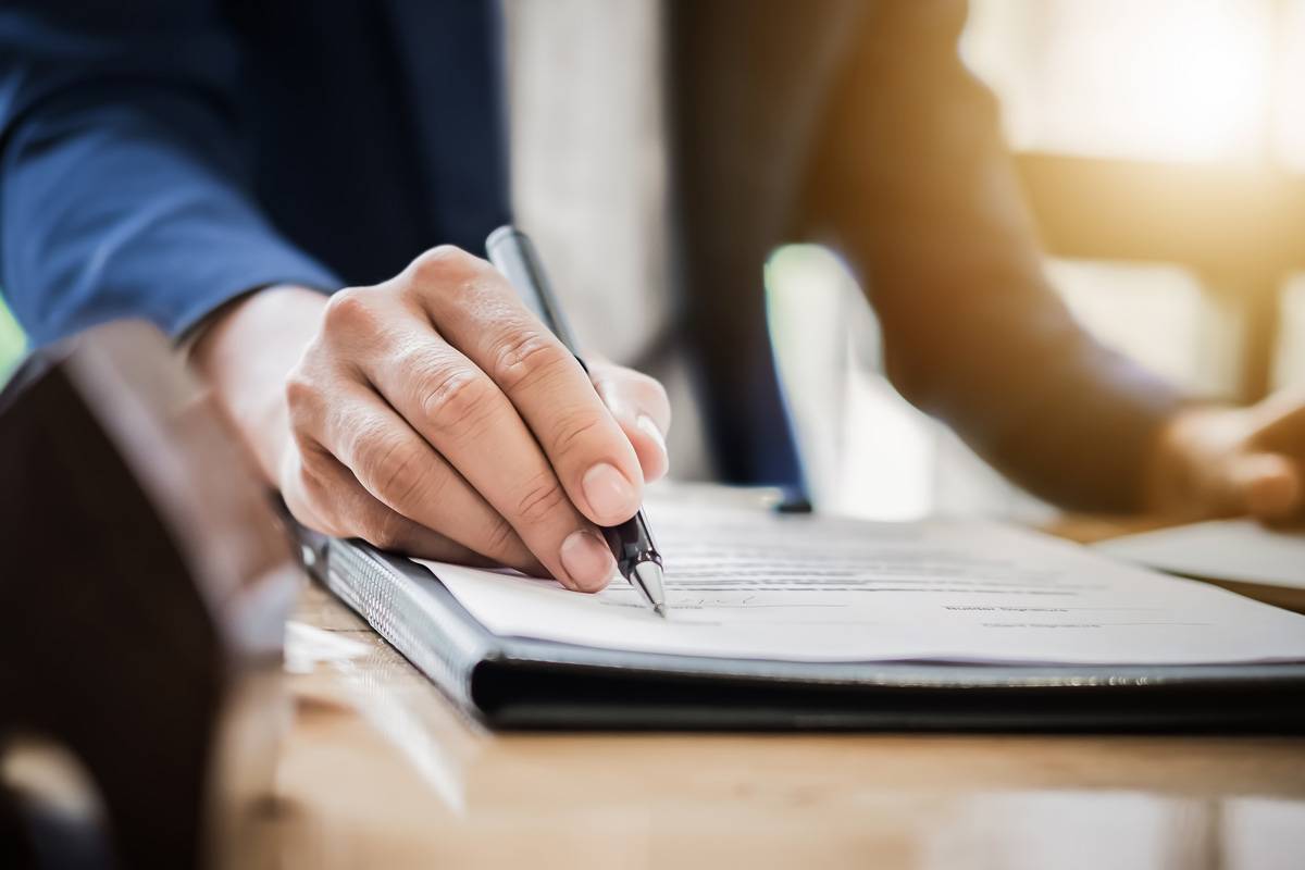 Female signing a document with sun shining in the background of office.