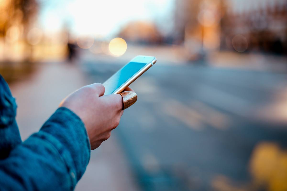 Women holding on to iphone standing on sidewalk.