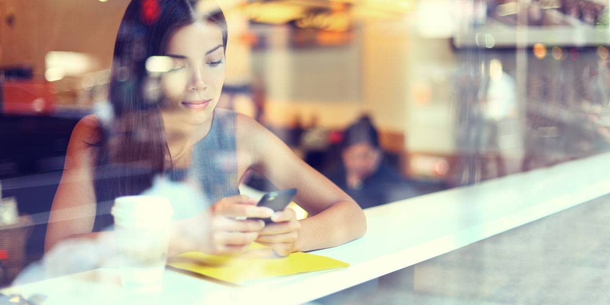 women wearing grey shirt looking down at phone in cafe